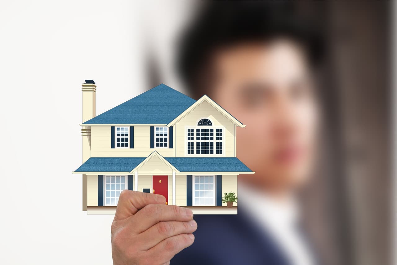 An image of a hand holding a model of a house with a blurred figure of a person in the background. The image symbolizes the concept of property management and real estate, with a focus on how AI and automation are transforming real estate operations